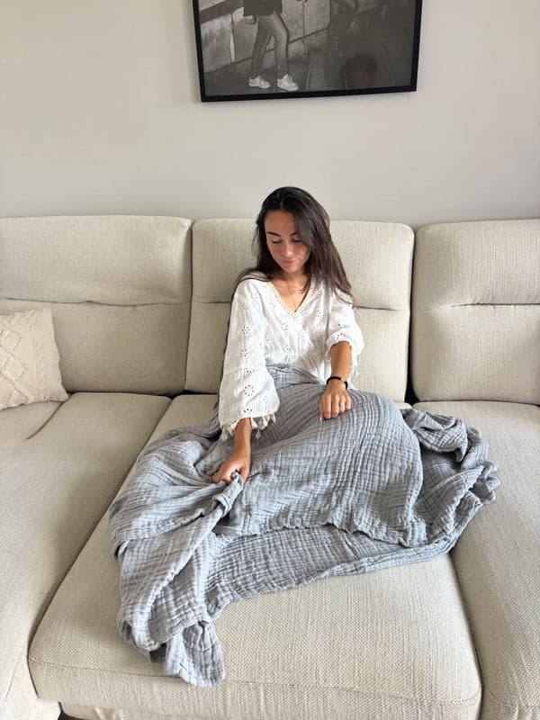 Kvinna i en ljus soffa med en grå muslinfilt över benen