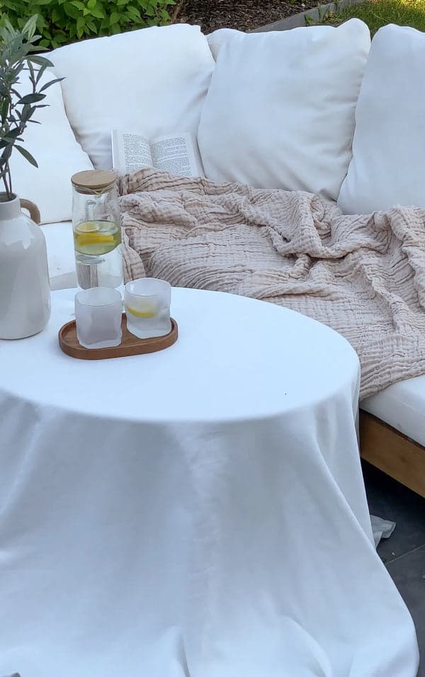 Beige muslinfilt på en trädgårdssoffa bredvid ett litet bord